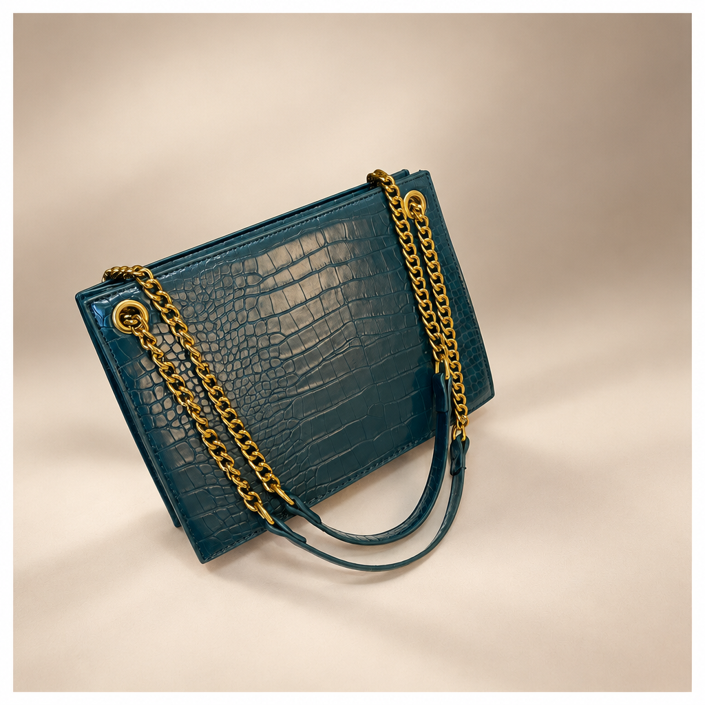 Blue crocodile-pattern shoulder bag with gold chain straps on a warm ivory and taupe studio background