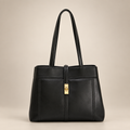 Black handbag with gold clasp on a warm ivory studio background