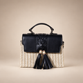 Cream woven box bag with black flap, top handle and twin tassels on warm ivory studio background