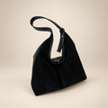 Black suede-look shoulder bag on a warm ivory studio background
