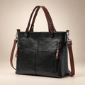 Black handbag with brown straps in a warm ivory and taupe studio setting, angled view