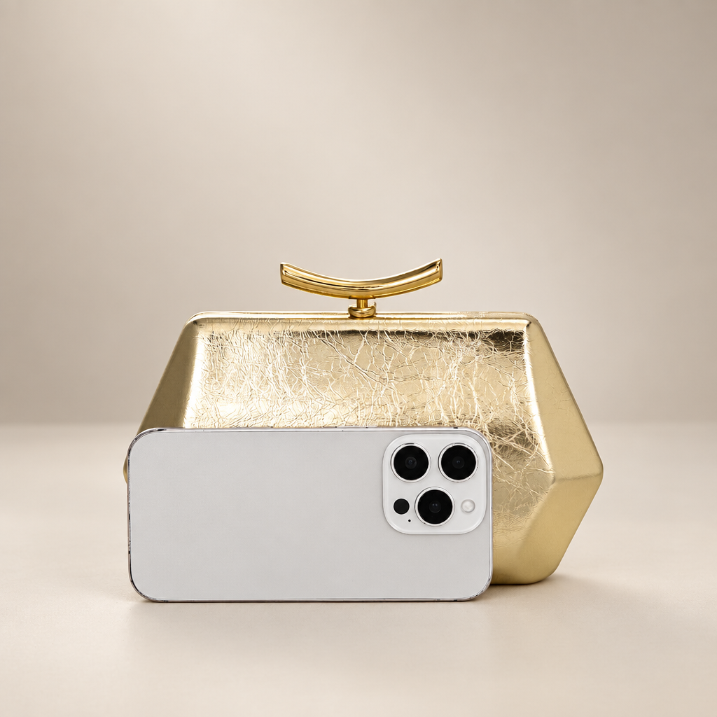 Gold faceted clutch with phone for scale on warm ivory studio background