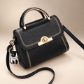 Black embroidered flap crossbody bag with top handle, long strap and key charm on a warm ivory and taupe studio background