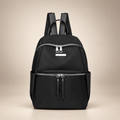 Black Oxford backpack with front zip pockets on a warm ivory studio background