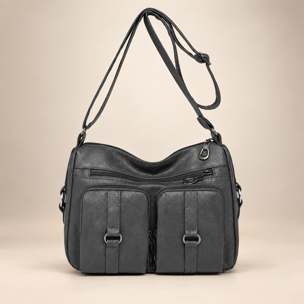 Gray PU crossbody bag with front zip and slip pockets on a warm ivory studio background