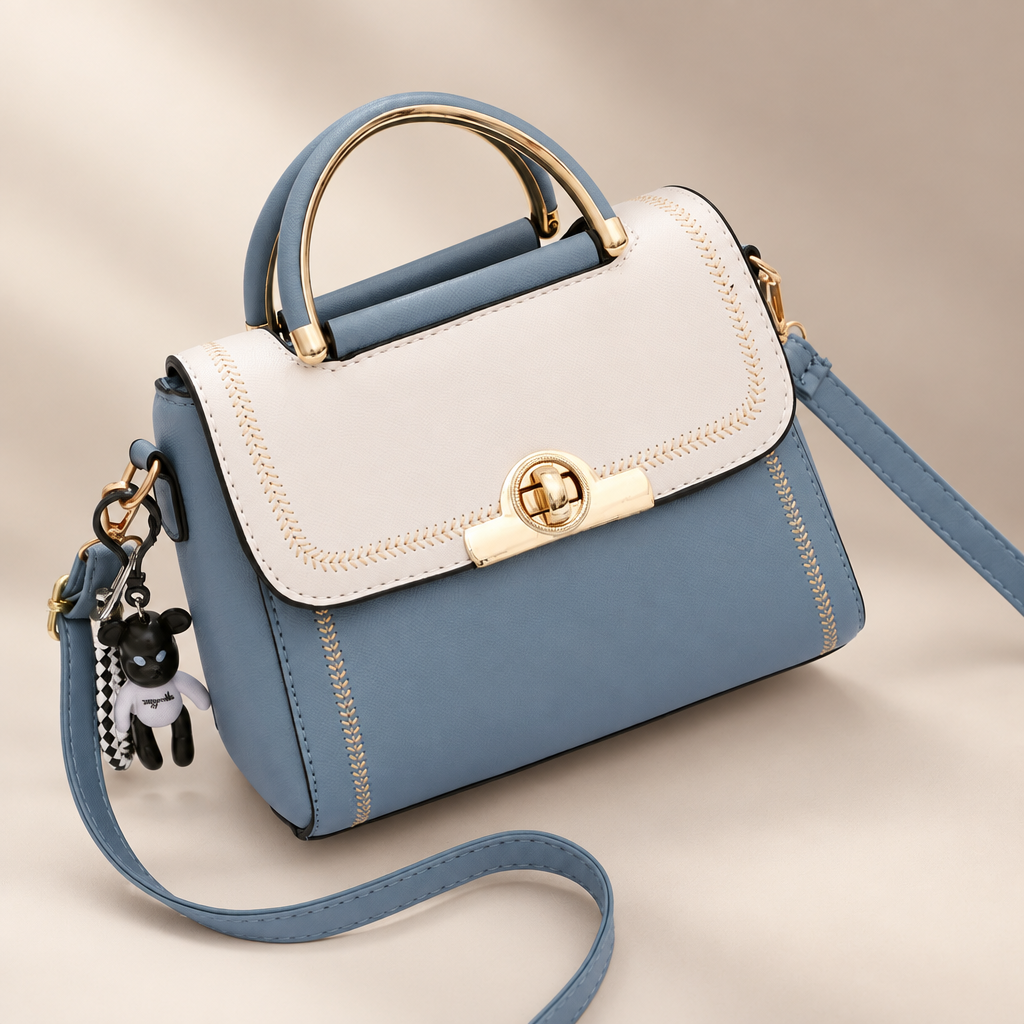 White And Blue colour-block embroidered crossbody bag with blue body, white flap, top handle and key charm on a warm ivory and taupe studio background