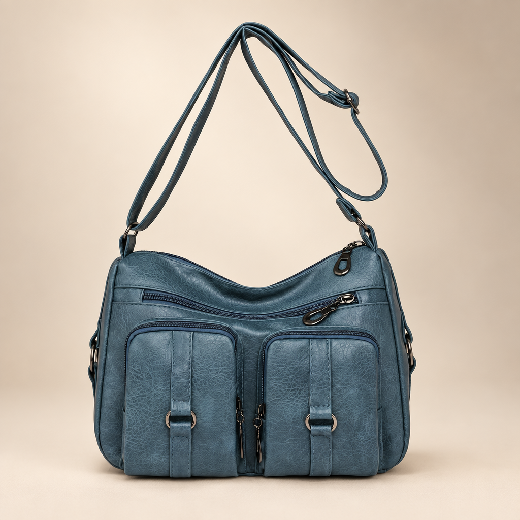 Lake blue PU crossbody bag with front zip and slip pockets on a warm ivory studio background