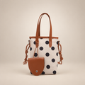 Cream polka-dot bucket bag with brown handles and pouch on a warm ivory studio background