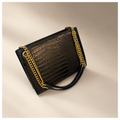 Black crocodile-pattern shoulder bag with gold chain straps on a warm ivory and taupe studio background