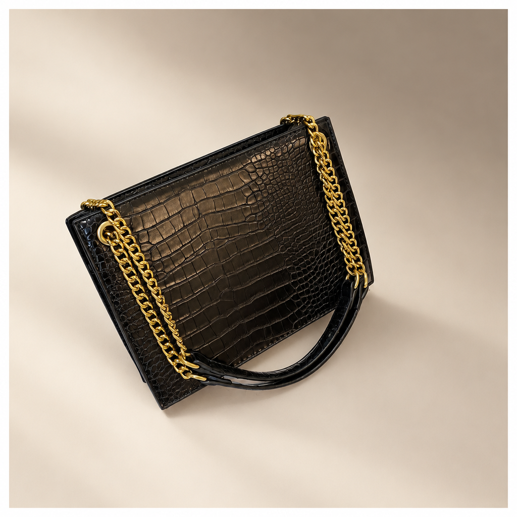 Black crocodile-pattern shoulder bag with gold chain straps on a warm ivory and taupe studio background