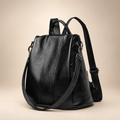 Black genuine leather backpack against a warm ivory and taupe studio background
